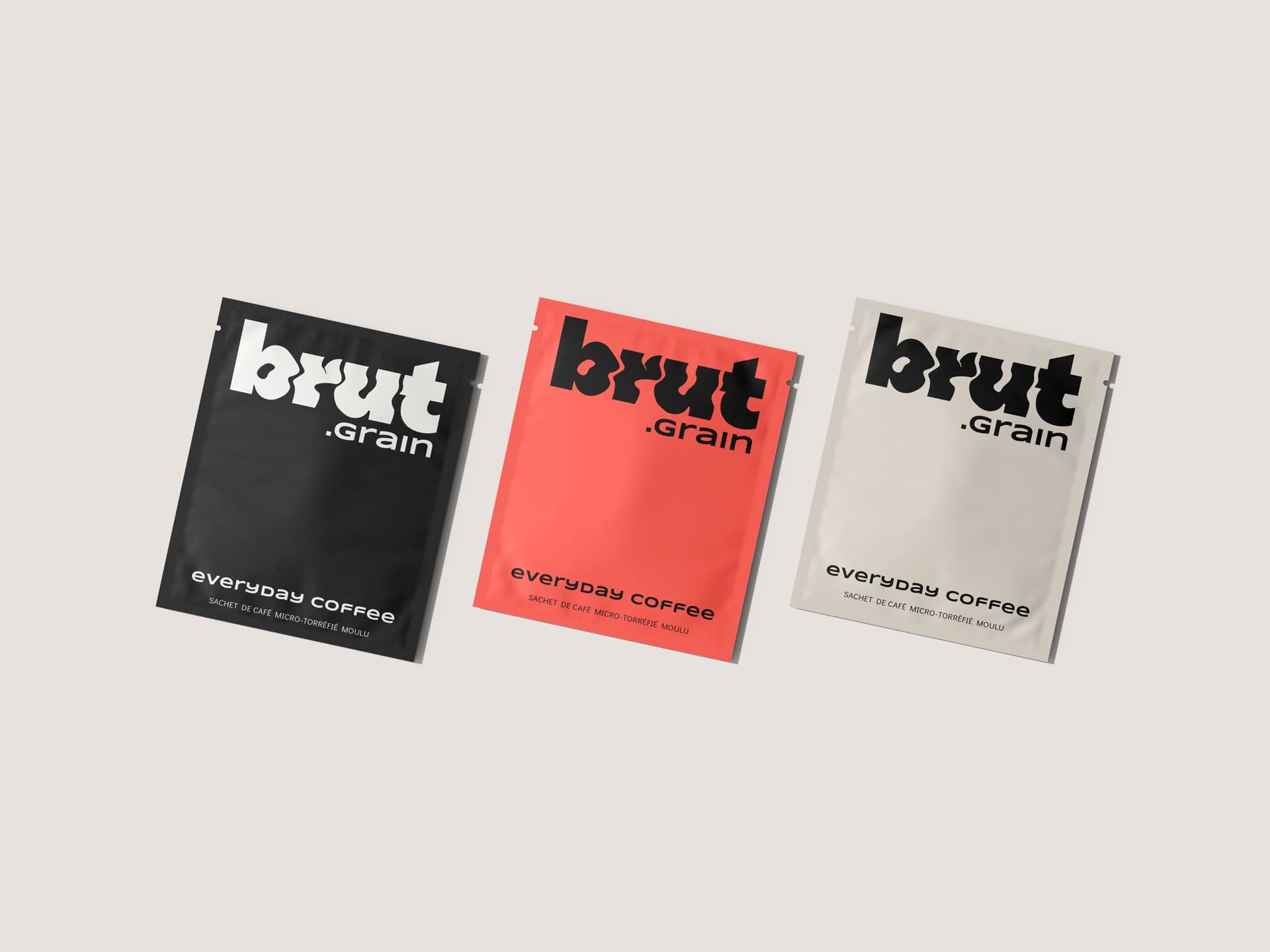 Les trois sachets brut.grain, noir, rouge et crème, posés sur fond crème